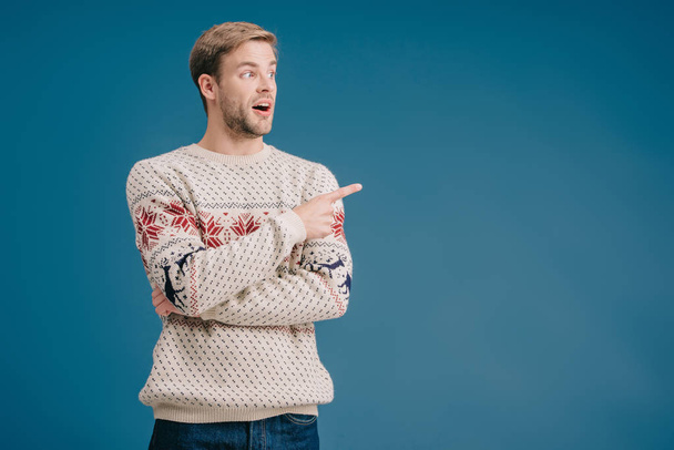 шокований чоловік взимку светр показує щось ізольоване на синьому
 - Фото, зображення