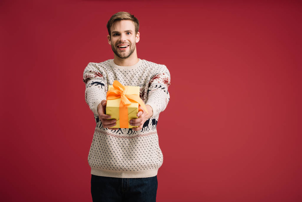 handsome cheerful man holding christmas gift isolated on red - Φωτογραφία, εικόνα