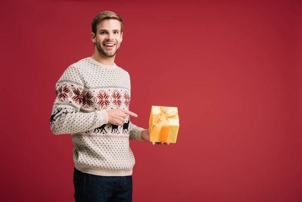 handsome man pointing at christmas gift box isolated on red - Φωτογραφία, εικόνα
