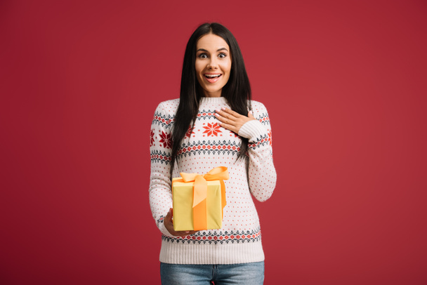mooie verrast vrouw Holding kerstcadeau geïsoleerd op rood - Foto, afbeelding