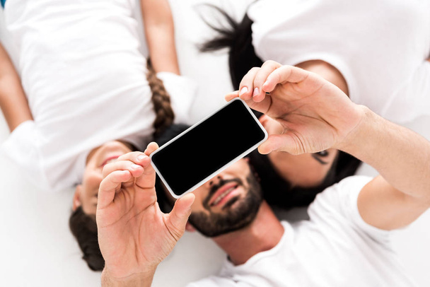 top view of happy bearded man holding smartphone with blank screen near wife and kid isolated on white  - Photo, Image