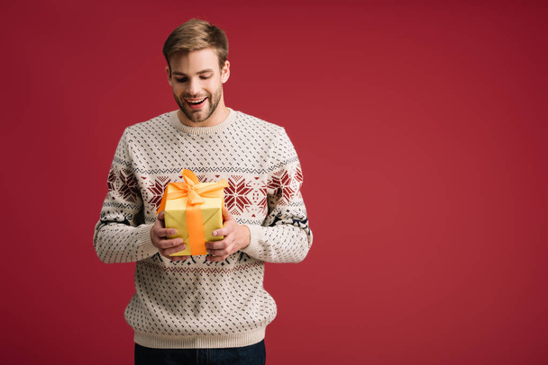 excited handsome man holding christmas gift box isolated on red - Fotó, kép