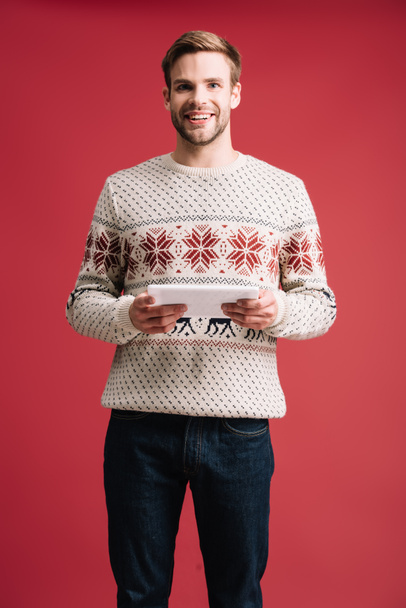 happy handsome man in winter sweater using digital tablet isolated on red - Foto, immagini