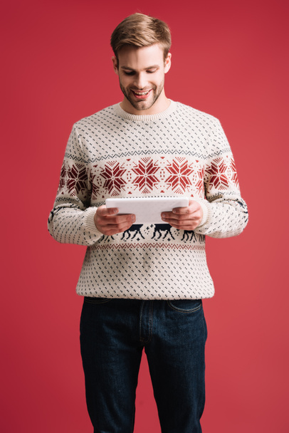 handsome smiling man in winter sweater using digital tablet isolated on red - Foto, afbeelding
