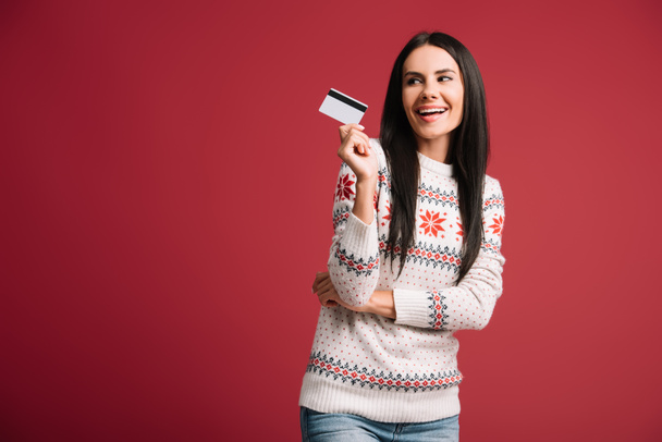 ευτυχισμένη γυναίκα με το χειμώνα πουλόβερ κατοχή πιστωτικής κάρτας, απομονώνονται σε κόκκινο  - Φωτογραφία, εικόνα