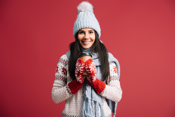 woman in winter hat, scarf and mittens holding coffee to go, isolated on red - Photo, Image