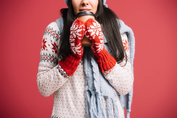 cropped view of woman in winter scarf and mittens holding coffee to go, isolated on red - Foto, imagen