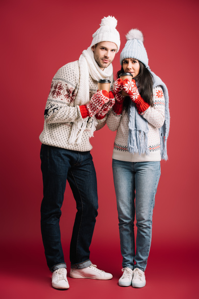 couple in winter sweaters, hats, scarves and mittens holding coffee to go isolated on blue - Foto, afbeelding