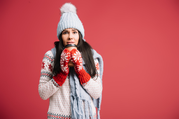 cold woman in winter hat, scarf and mittens holding coffee to go, isolated on red - 写真・画像