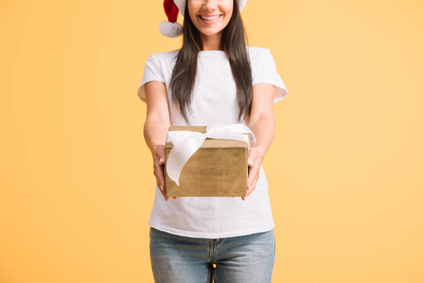 cropped view of smiling woman in santa hat holding christmas gift box isolated on yellow - Fotografie, Obrázek