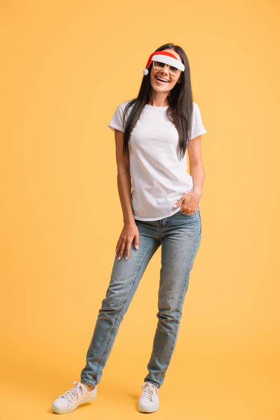 cheerful woman in white t-shirt and glasses with santa hat isolated on yellow - Foto, Imagem
