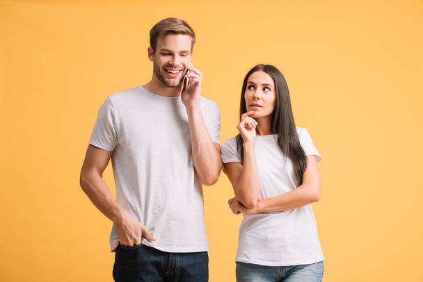 boyfriend talking on smartphone while woman listen in, isolated on yellow - Fotoğraf, Görsel