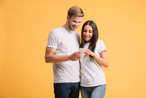 sonriente pareja usando smartphone aislado en amarillo
 - Foto, Imagen