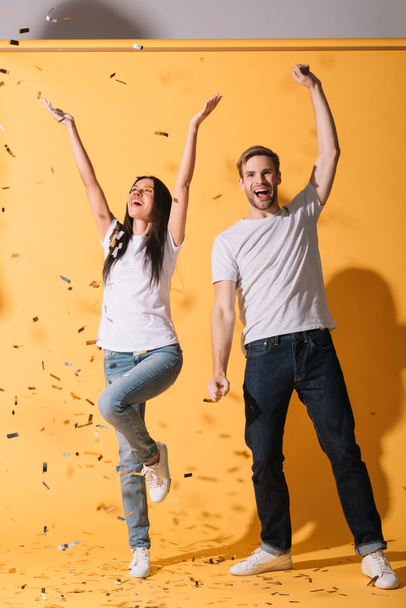 excited couple dancing on yellow with golden confetti - Фото, зображення