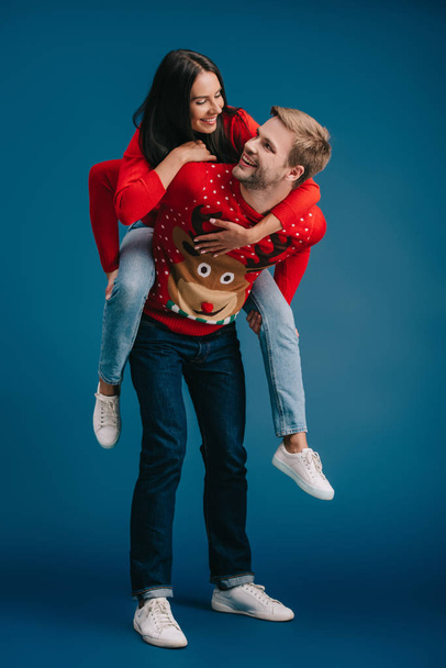 beautiful couple in christmas sweaters piggybacking isolated on blue - Fotografie, Obrázek