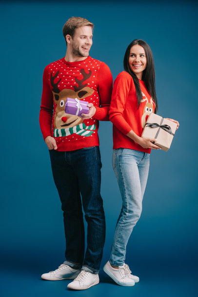 couple in red sweaters holding christmas gifts isolated on blue - Foto, Imagem