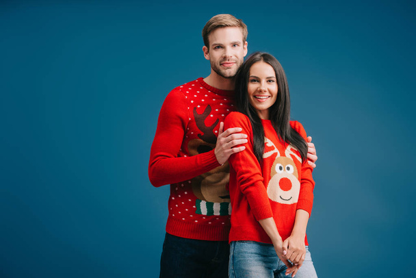 beautiful happy couple in christmas sweaters hugging isolated on blue - Photo, Image