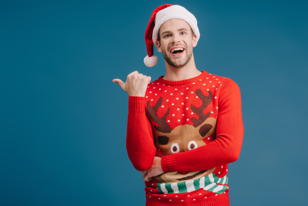 izgatott jóképű férfi Santa kalap és a karácsonyi pulóver mutatott elszigetelt kék - Fotó, kép