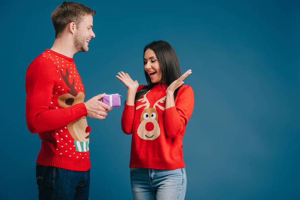 man presenting christmas gift box to surprised woman isolated on blue - Photo, Image