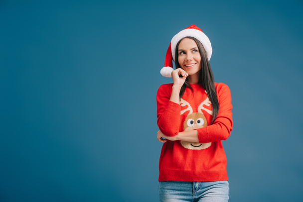 smiling woman posing in santa hat and christmas sweater isolated on blue - Valokuva, kuva