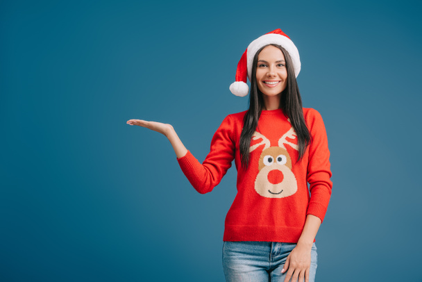 smiling woman in santa hat showing something isolated on blue - Zdjęcie, obraz