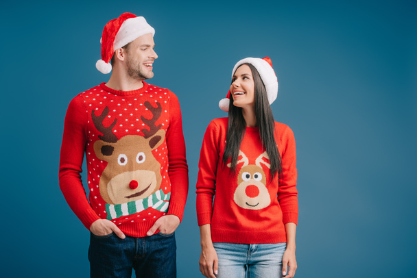 laughing couple posing in santa hats and sweaters isolated on blue - Foto, immagini