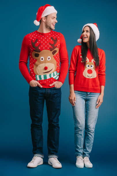 beautiful couple posing in santa hats and sweaters on blue - Фото, зображення