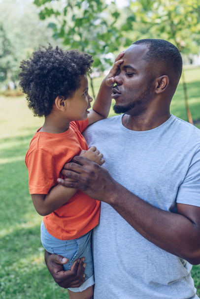bonito afro-americano menino tocando nariz de pai enquanto sentado em seus braços
 - Foto, Imagem