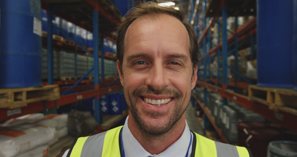 Portrait close up of a middle aged Caucasian male warehouse manager looking to camera smiling in a storage warehouse - Metraje, vídeo