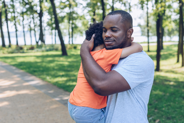 felice padre afroamericano che tiene e abbraccia adorabile figlio nel parco
 - Foto, immagini