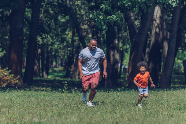 Χαρούμενος Αφρικάνος πατέρας και γιος τρέχουν ενώ διασκεδάζουν στο πάρκο - Φωτογραφία, εικόνα
