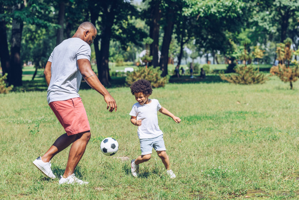 joven afroamericano padre jugando fútbol con lindo hijo en parque
 - Foto, Imagen