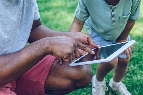bijgesneden beeld van Afrikaanse Amerikaanse vader en zoon met behulp van digitale tablet in het park - Foto, afbeelding