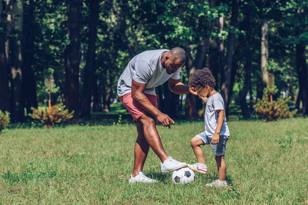 joven afroamericano padre enseñanza hijo jugando fútbol en parque
 - Foto, Imagen