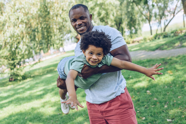 jovem afro-americano homem segurando adorbale filho enquanto se divertindo no parque
 - Foto, Imagem