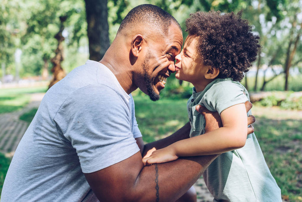 cute african american boy kissing happy father while having fun in park - Fotografie, Obrázek