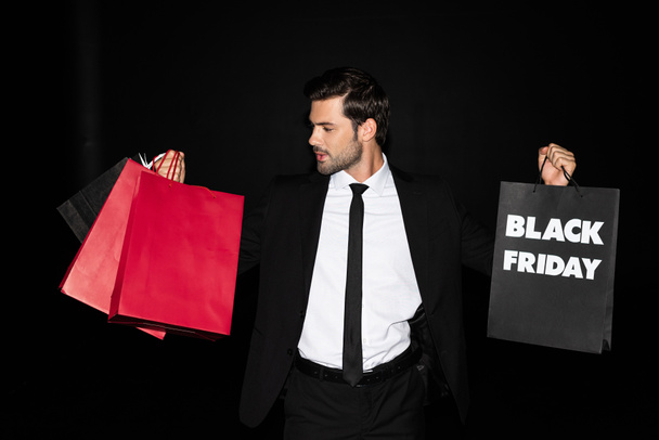 elegant man holding shopping bags with black friday sign, isolated on black  - Fotoğraf, Görsel