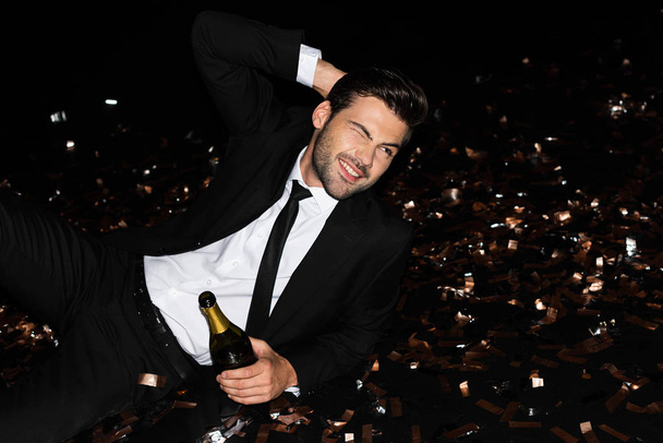 elegant man with champagne bottle lying on floor with golden confetti for holiday - Foto, immagini