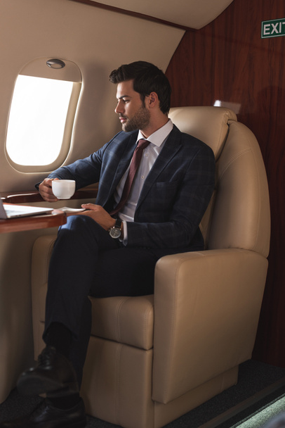 serio uomo d'affari in giacca e cravatta bere caffè in aereo durante il viaggio d'affari
 - Foto, immagini
