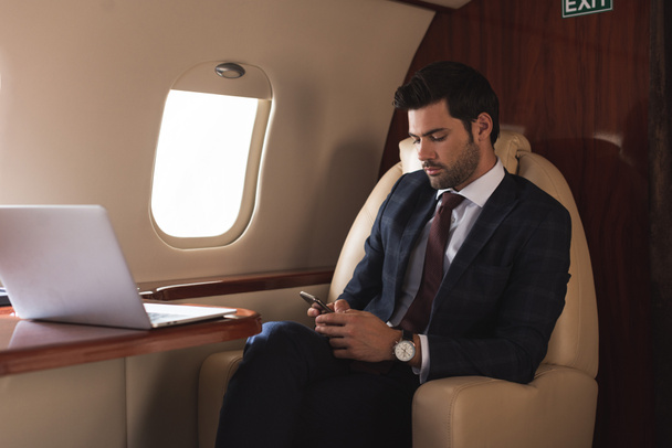 бизнесмен работает на смартфоне и ноутбуке в самолете во время деловой поездки
  - Фото, изображение