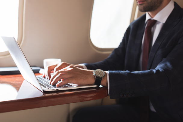 vue recadrée de l'homme d'affaires tapant sur un ordinateur portable dans un avion pendant un voyage d'affaires
  - Photo, image