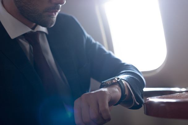 cropped view of businessman looking at watch while sitting in airplane - 写真・画像