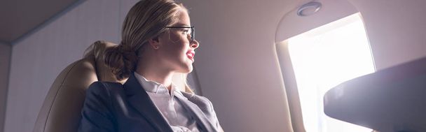 attractive businesswoman looking at window in plane during business trip - Фото, изображение