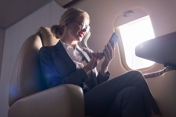 zmartwiony bizneswoman mówi na smartfonie w samolocie podczas podróży służbowej  - Zdjęcie, obraz