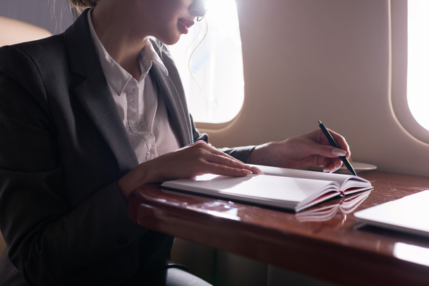 cropped view of businesswoman working with documents in plane during business trip - 写真・画像