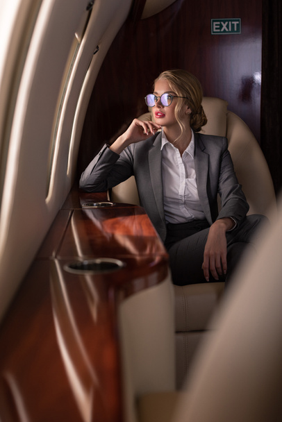 beautiful businesswoman in glasses sitting in airplane during business trip - Фото, изображение