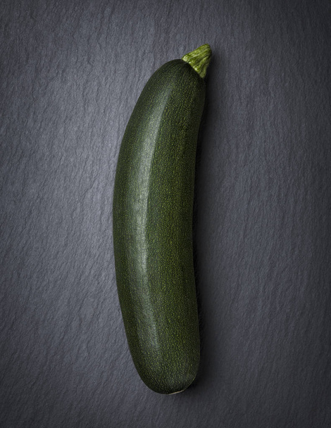 One courgette isolated on dark stone. - 写真・画像