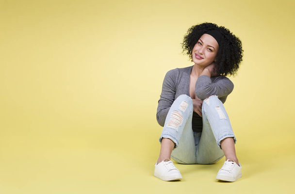 Happy smiling woman sitting on yellow isolated background with empty copy space. - Фото, зображення