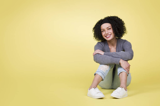Joyful smiling woman sitting on yellow isolated background with empty copy space. - Photo, image