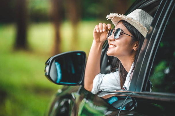 Szczęśliwy kobieta ręka trzyma kapelusz na zewnątrz otwarte okno samochód z zielonym  - Zdjęcie, obraz